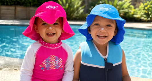 2 enfants assis au bord d'une piscine avec un ensemble anti-UV Plouf, un maillot de bain flottant Plouf et un bob anti-UV Plouf